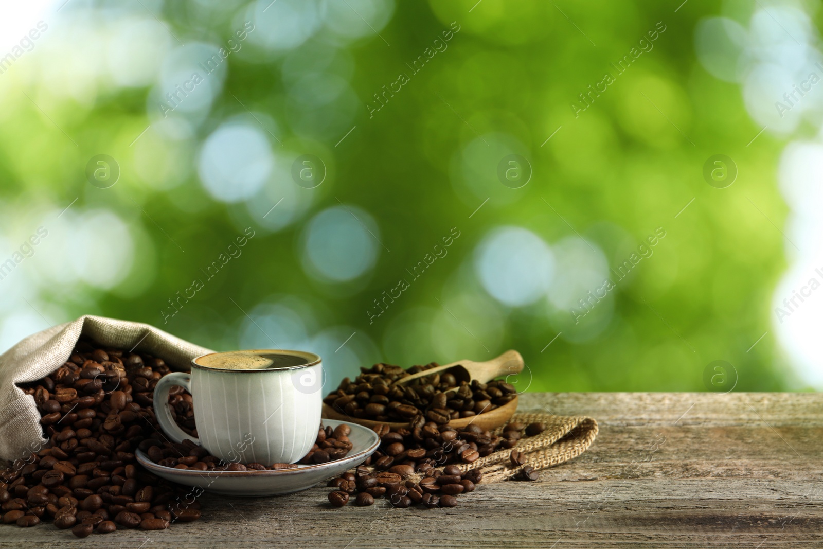 Image of Cup of aromatic hot coffee and beans on wooden table outdoors. Space for text