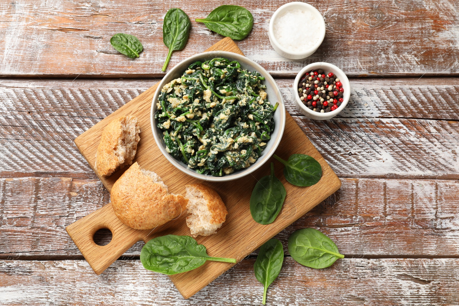 Photo of Tasty spinach dip with egg in bowl, bread and spices on wooden table, top view