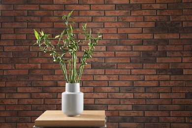 Vase with bamboo stems on table against brick wall, space for text