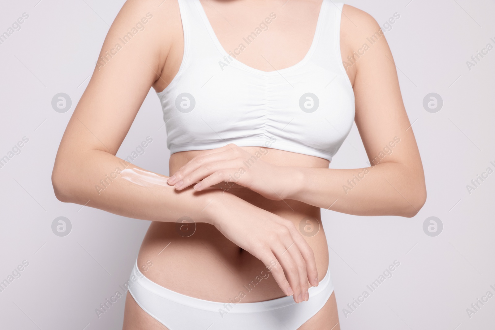 Photo of Woman applying body cream onto arm on light grey background, closeup