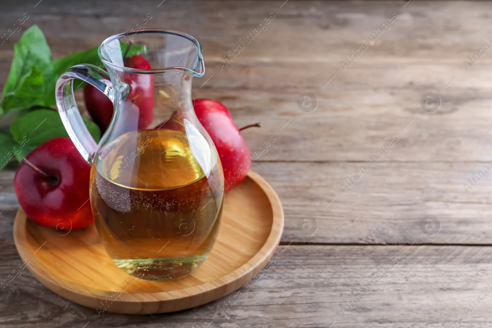 Photo of Jug of tasty juice and fresh red apples on wooden table, space for text