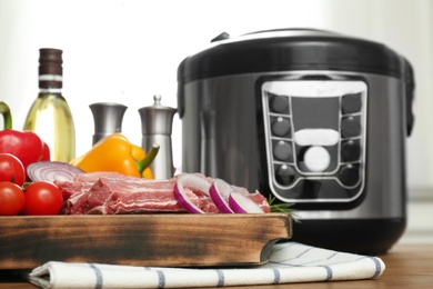 Photo of Modern multi cooker and products on wooden table in kitchen