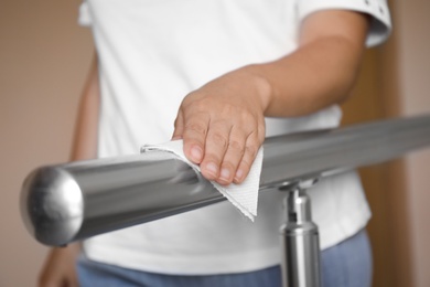 Photo of Woman cleaning metal railing with tissue paper, closeup