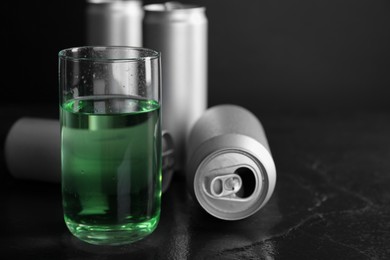 Photo of Energy drink in glass and aluminium cans on black table, closeup. Space for text