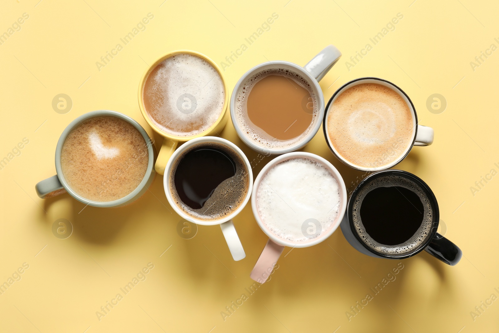 Photo of Many different cups with aromatic coffee on yellow table, flat lay