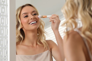 Photo of Beautiful makeup. Smiling woman with brush in front of mirror indoors