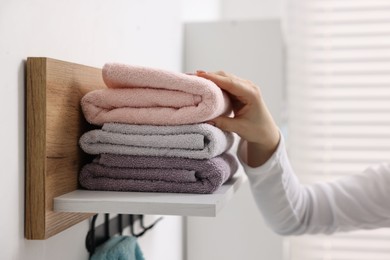 Woman stacking clean towels on shelf indoors, closeup