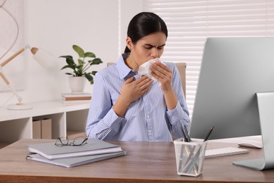 Photo of Woman with tissue coughing at table in office. Cold symptoms