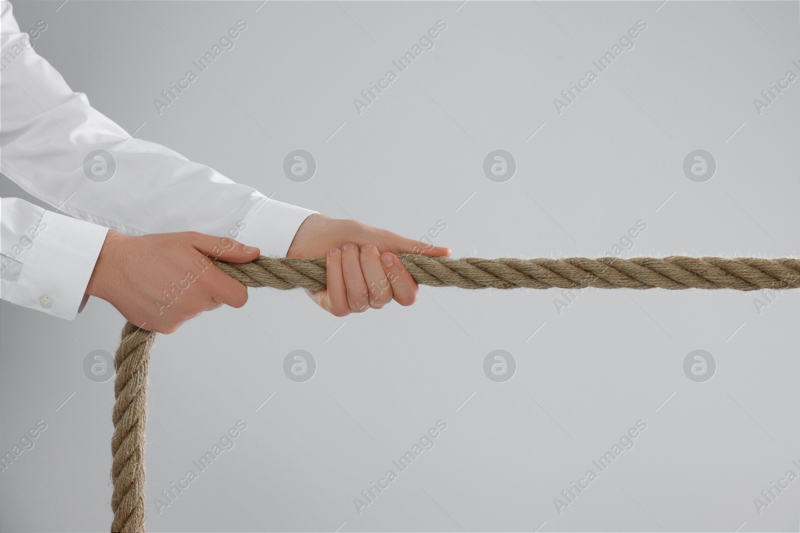 Photo of Dispute concept. Man pulling rope on light grey background, closeup