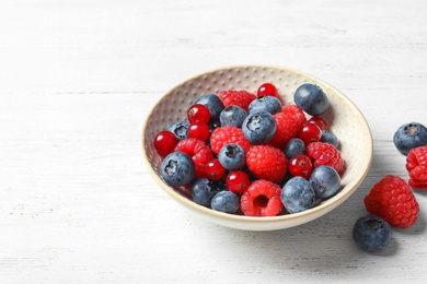 Photo of Bowl with raspberries, red currant and blueberries on wooden table