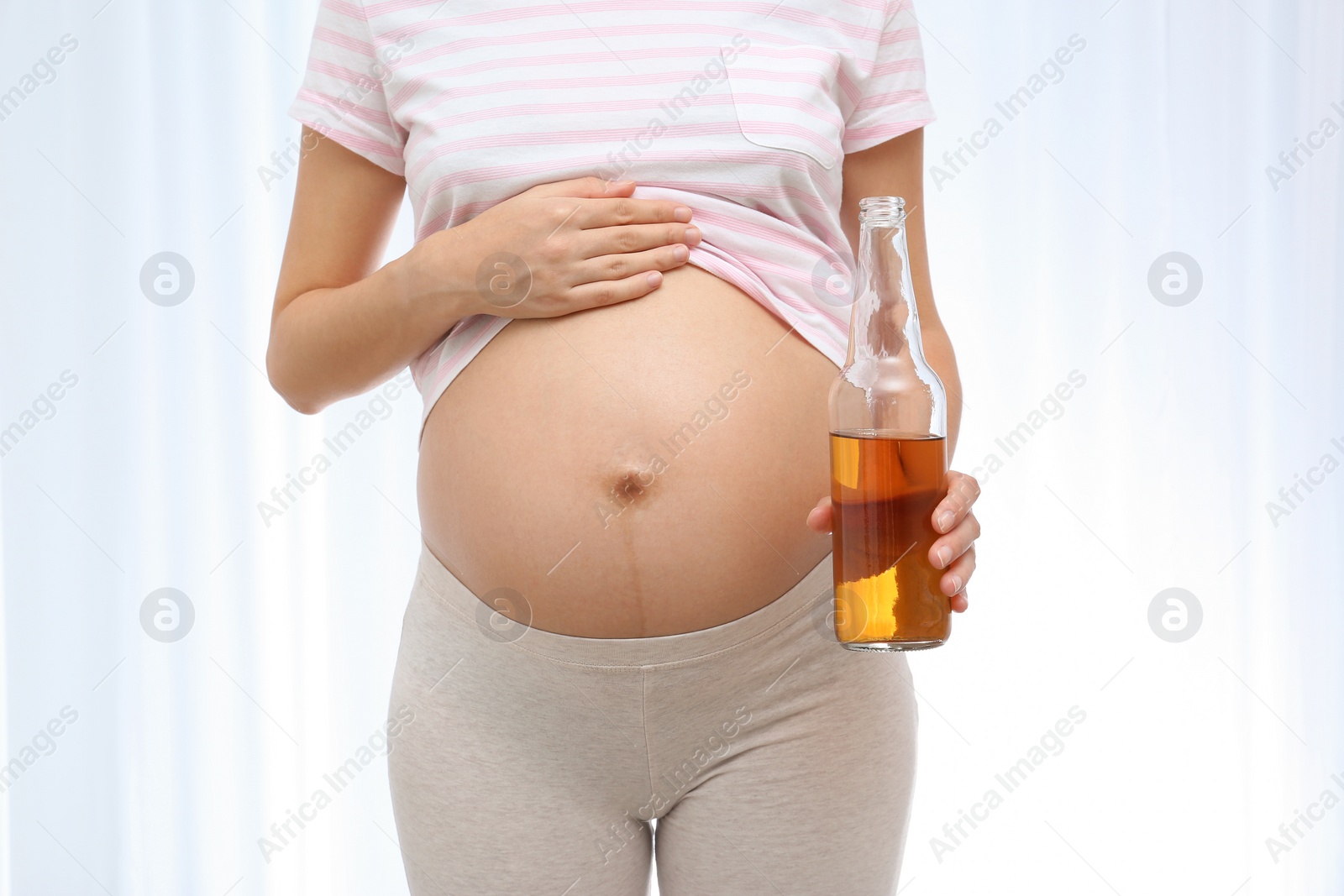 Photo of Pregnant woman with bottle of whiskey on light background. Alcohol addiction