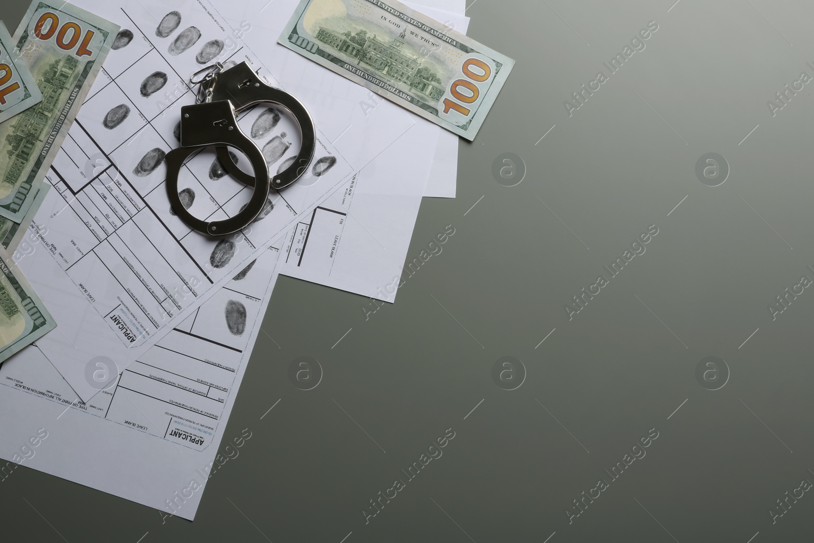 Photo of Money, handcuffs and fingerprint record sheets on grey background, top view with space for text. Criminal investigation