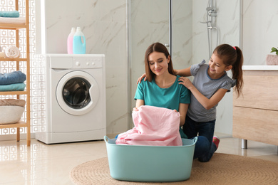 Mother and little daughter with clean laundry in bathroom