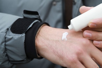 Man applying cream from tube onto hand, closeup. Winter care