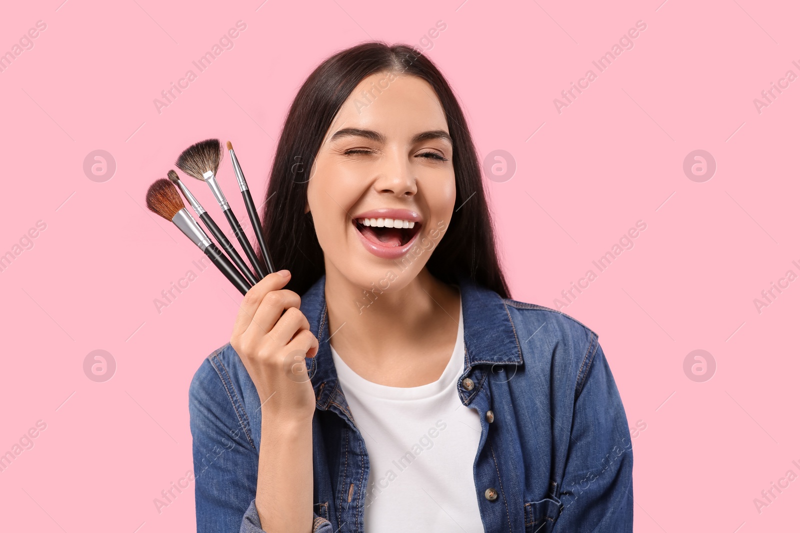 Photo of Happy woman with different makeup brushes on pink background