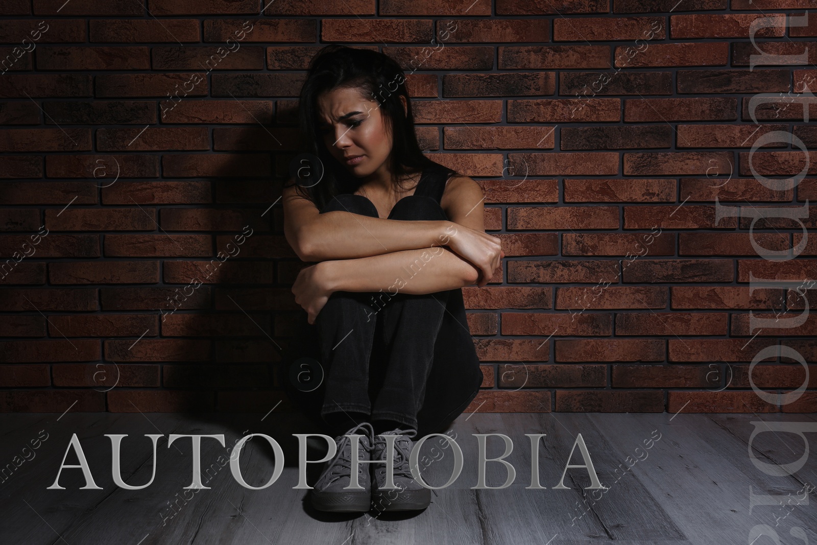 Image of Depressed young woman sitting alone near brick wall. Autophobia - fear of isolation