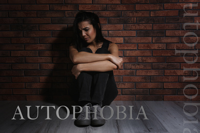 Image of Depressed young woman sitting alone near brick wall. Autophobia - fear of isolation