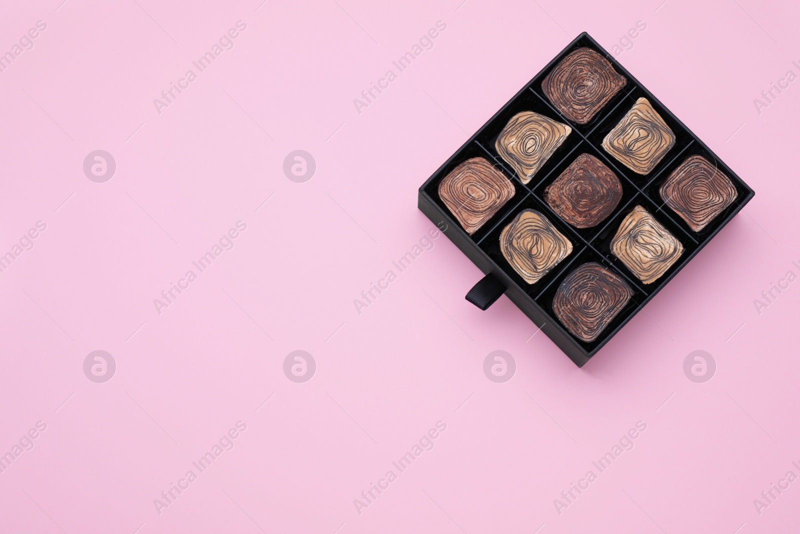 Photo of Box of tasty chocolate candies on pink background, top view. Space for text