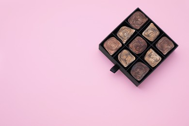 Box of tasty chocolate candies on pink background, top view. Space for text