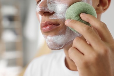 Photo of Young man washing off face mask with sponge in bathroom, closeup