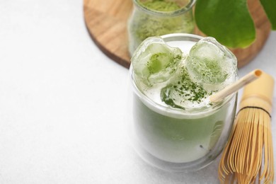 Photo of Glass of tasty iced matcha latte, leaf and bamboo whisk on white table, closeup. Space for text