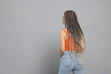 Photo of Beautiful woman with long african braids on grey background, back view. Space for text