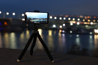 Taking photo with smartphone on tripod near river at night