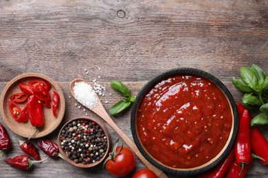 Flat lay composition with bowl of chili sauce and ingredients on wooden table. Space for text