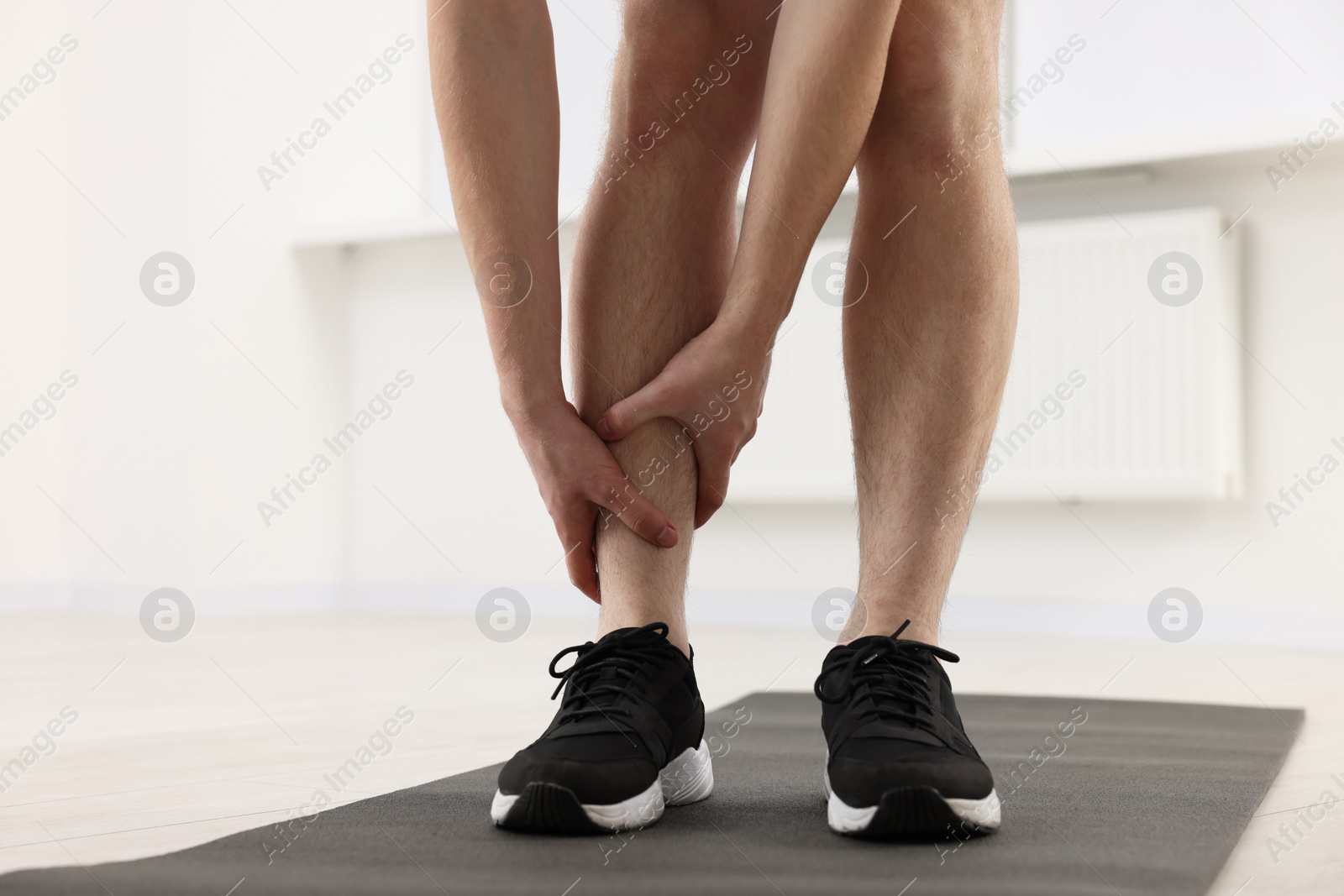 Photo of Man suffering from leg pain on mat indoors, closeup