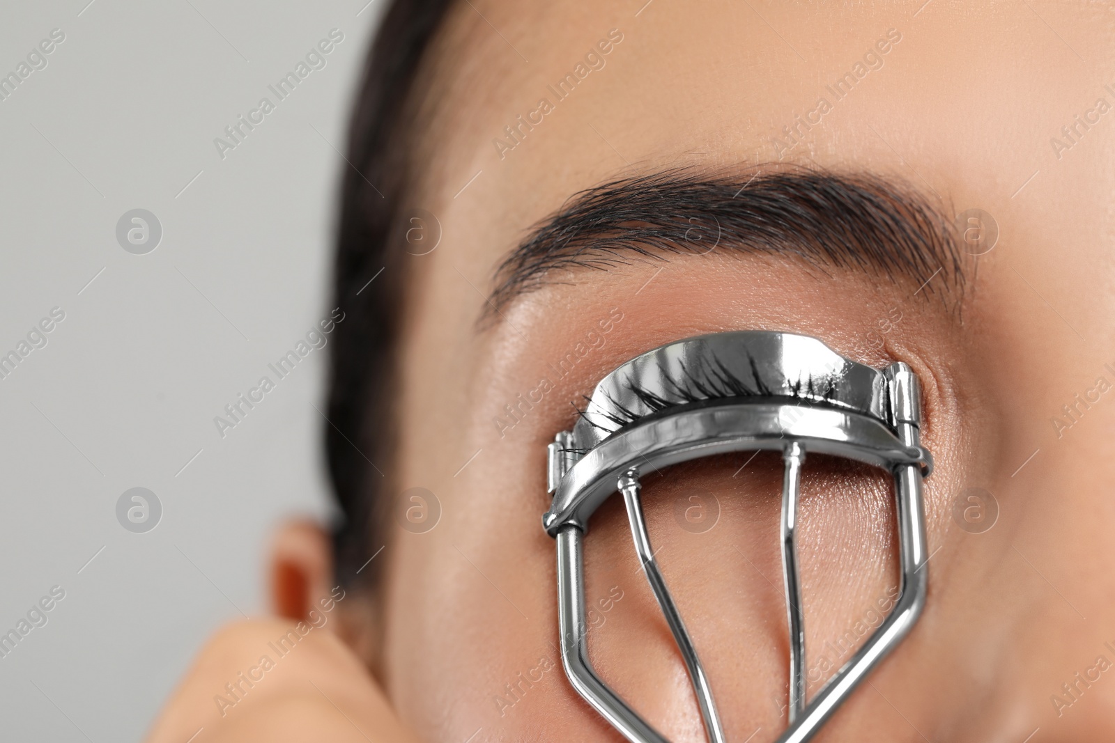 Photo of Young woman using eyelash curler on light grey background, closeup