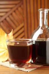 Bottle and glass of tasty maple syrup on wooden table