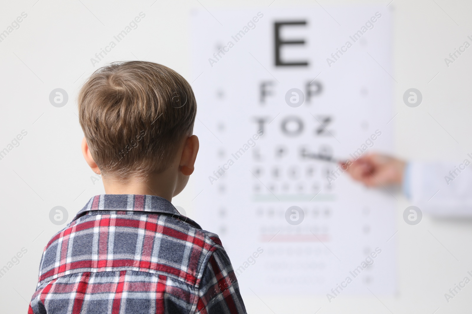 Photo of Ophthalmologist testing little boy's vision in clinic, back view