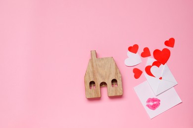 Photo of Long-distance relationship concept. House model, love letter and hearts on pink background, flat lay. Space for text