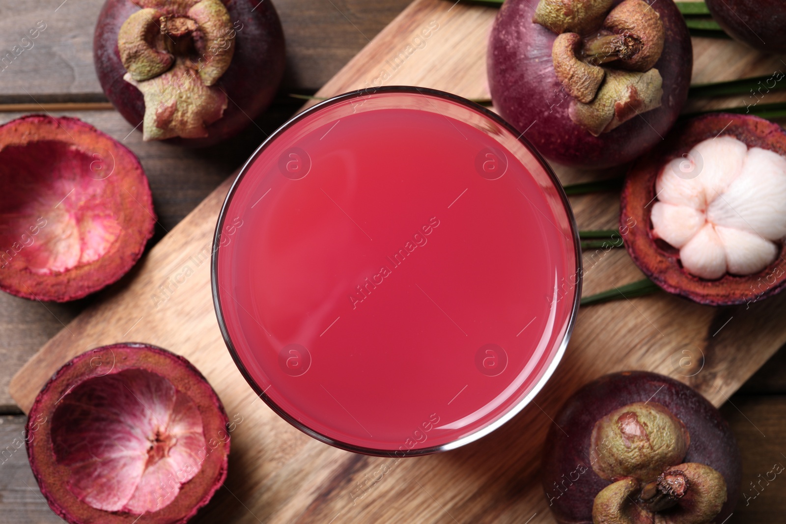 Photo of Delicious fresh mangosteen juice in glass on wooden table, flat lay