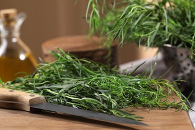 Fresh tarragon leaves and knife on wooden board, closeup