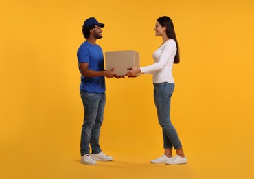 Photo of Smiling courier giving parcel to receiver on orange background