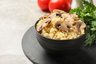 Delicious bulgur with mushrooms in bowl on gray table, closeup. Space for text