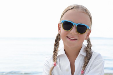 Little girl wearing sunglasses at beach on sunny day. Space for text