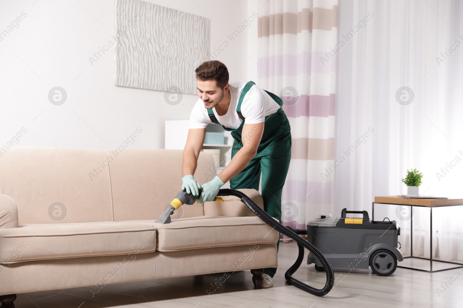 Photo of Professional janitor cleaning sofa in living room