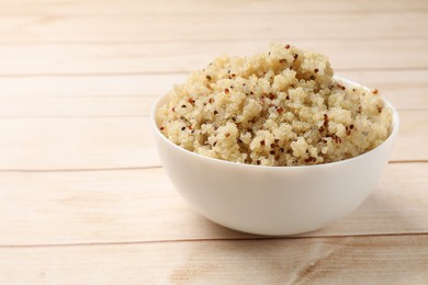 Photo of Tasty quinoa porridge in bowl on light wooden table, closeup. Space for text