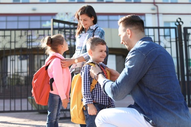 Photo of Young parents saying goodbye to their little children near school