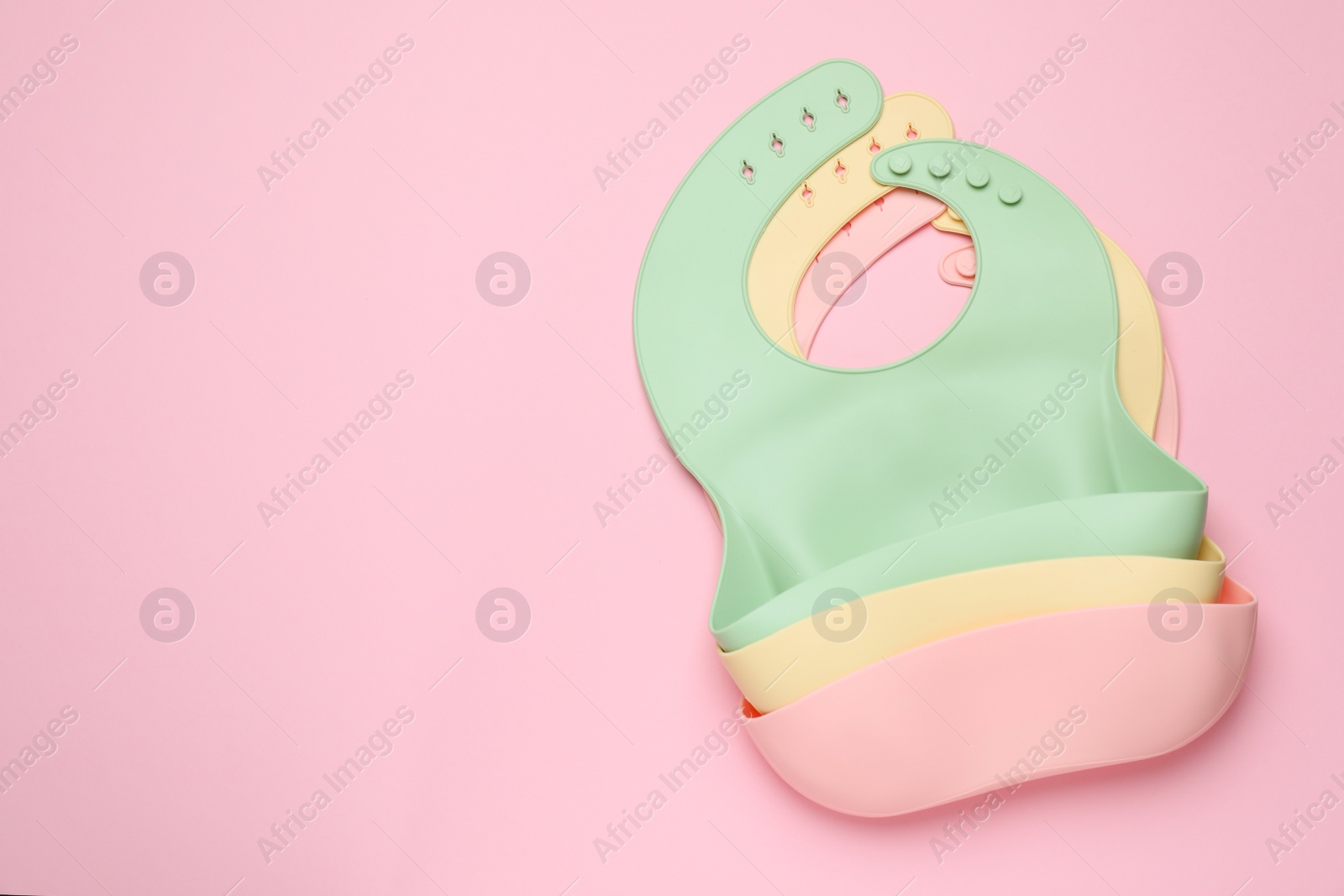 Photo of Three silicone baby bibs on pink background, top view. Space for text