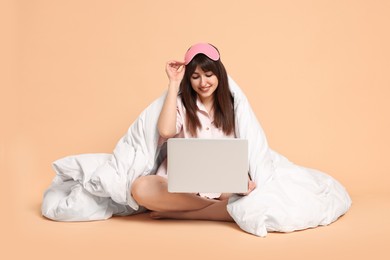 Photo of Happy woman with pyjama and blanket holding laptop on beige background