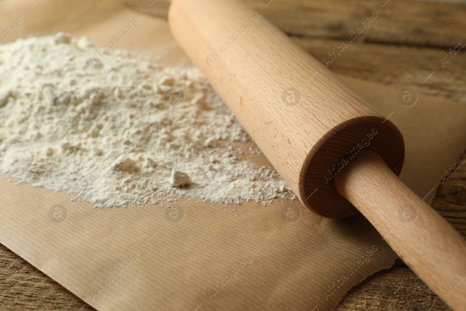 Photo of Parchment with flour and rolling pin on wooden table, closeup