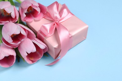 Photo of Beautiful gift box with bow and tulips on light blue background, closeup