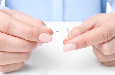 Photo of Woman threading sewing needle at table, closeup