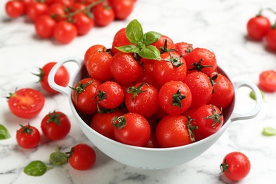Photo of Fresh wet cherry tomatoes with basil leaves on white marble table