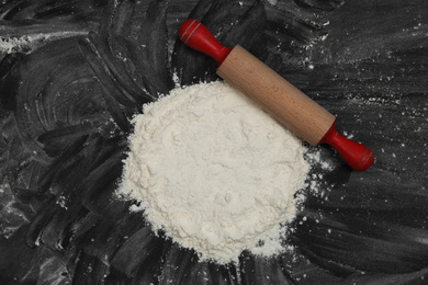 Flour and rolling pin on black table, top view