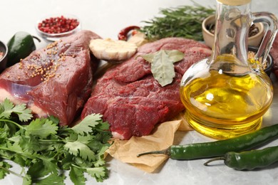 Photo of Pieces of raw beef meat, parsley and spices on light grey marble table, closeup