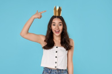 Photo of Beautiful young woman pointing at princess crown on light blue background